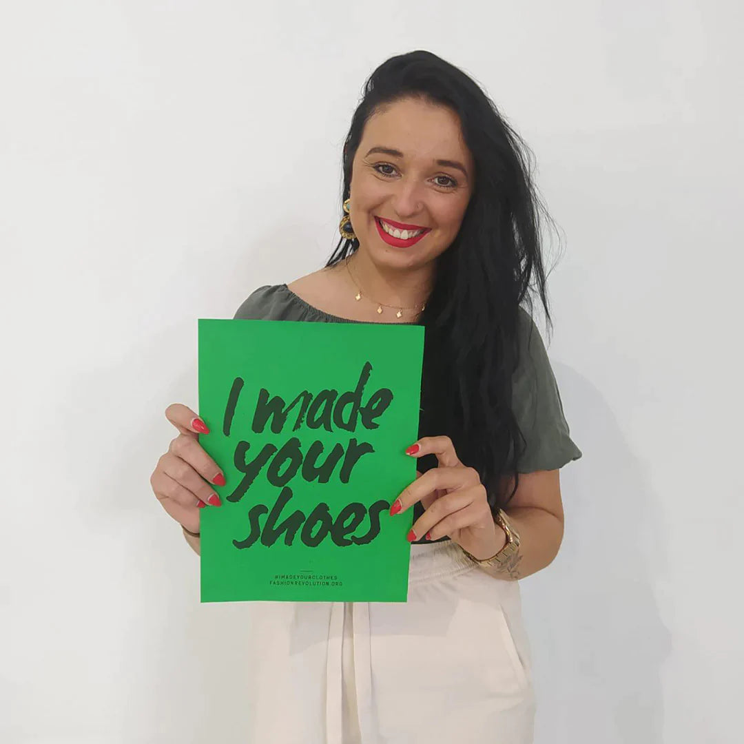 A woman in Trash Planet's ethical vegan sneaker manufacturing facility holding up an "I made your shoes" poster as part of the Fashion Revolution week.